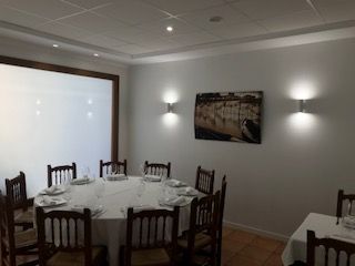 Comedor con mesa redonda puesta para comer, apliques de pared y un gran ventanal.