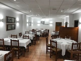 Comedor vacío de un restaurante con manteles blancos, sillas de madera y suelo de baldosas.