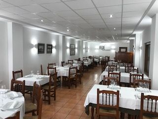 Comedor vacío con manteles blancos, sillas de madera y apliques de pared luminosos.