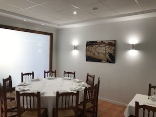 Comedor con mesa redonda puesta para comer, sillas de madera, apliques de pared y un cuadro enmarcado.