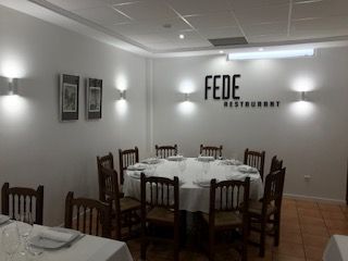 Comedor con mesa redonda preparada para varios comensales, paredes blancas y letrero que dice 