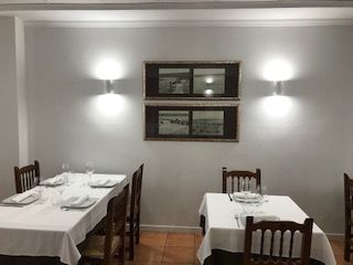 Comedor con manteles blancos, sillas de madera, apliques de pared y un espejo enmarcado o una obra de arte.