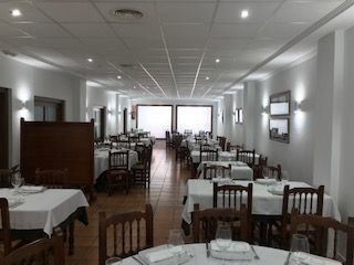 Comedor luminoso con filas de mesas, sillas y manteles blancos bajo luces de techo.