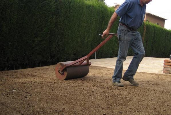 Un hombre está usando un rodillo para rodar tierra en el suelo.