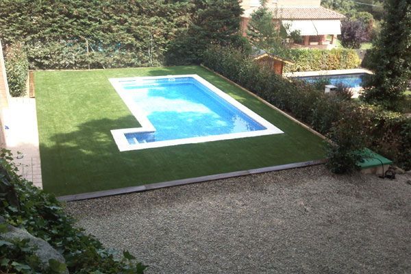 Una gran piscina rodeada de césped y arbustos.
