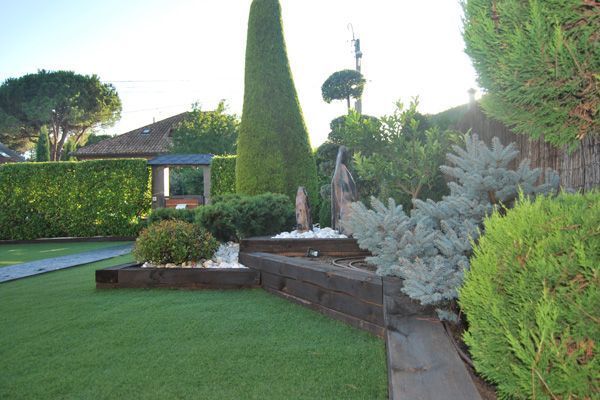 Un exuberante jardín verde con árboles y arbustos y una casa al fondo.