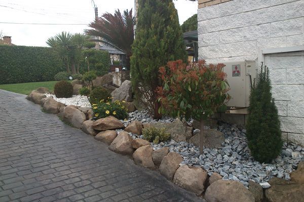 Un camino de ladrillo que conduce a una casa con rocas y plantas.