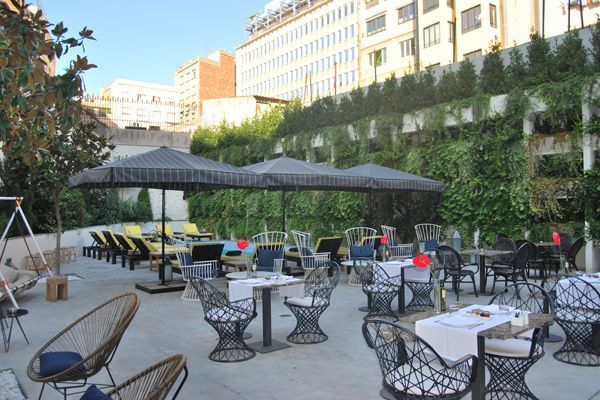 Un patio con mesas, sillas y sombrillas frente a un edificio.