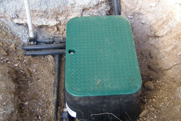 Una caja verde está tirada en la tierra al lado de una tubería.