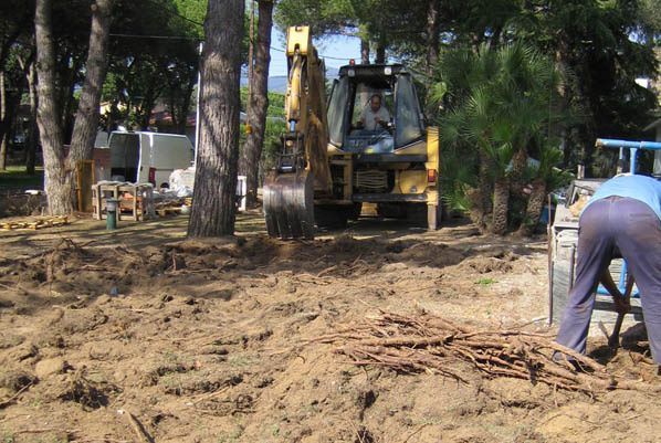 Un hombre está cavando en la tierra delante de una excavadora.