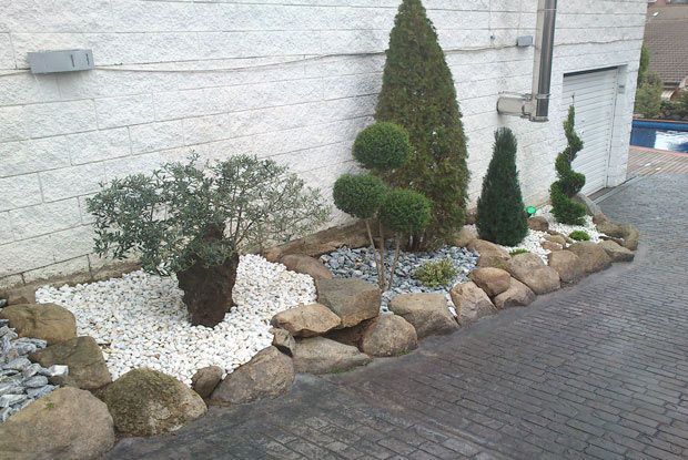 Un jardín con árboles y rocas frente a un edificio blanco.