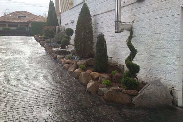 Una hilera de árboles y rocas al costado de un edificio.