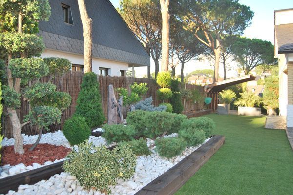 Un jardín con árboles y arbustos frente a una casa.