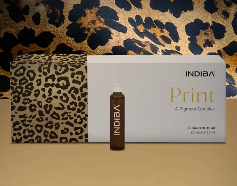 Caja de INDIBIA Print A-Pigment Complex con un vial, sobre un fondo de estampado de leopardo y una superficie dorada.