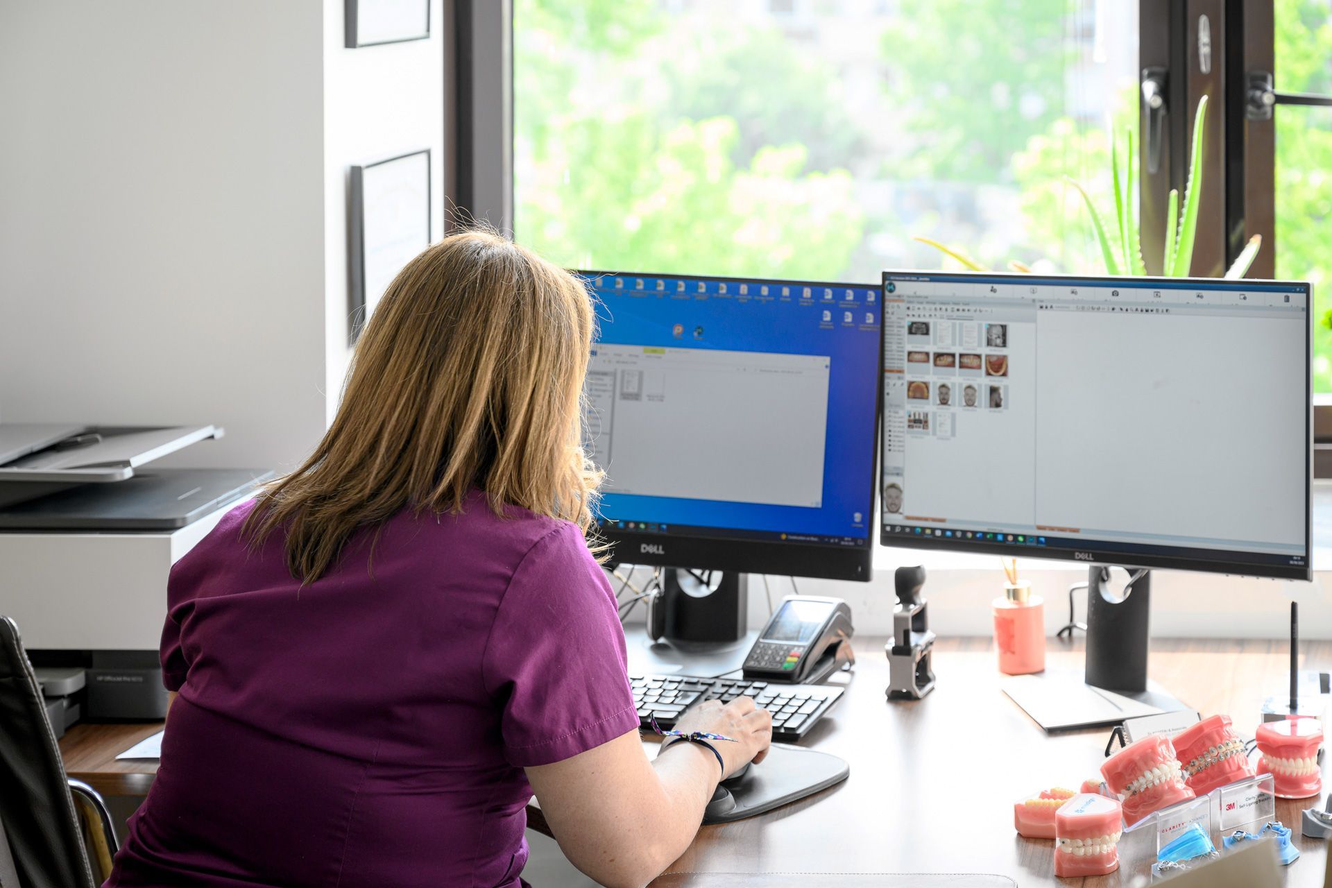 Membre de l'équipe du cabinet dentaire en train de regarder des fichiers sur un ordinateur avec deux moniteurs