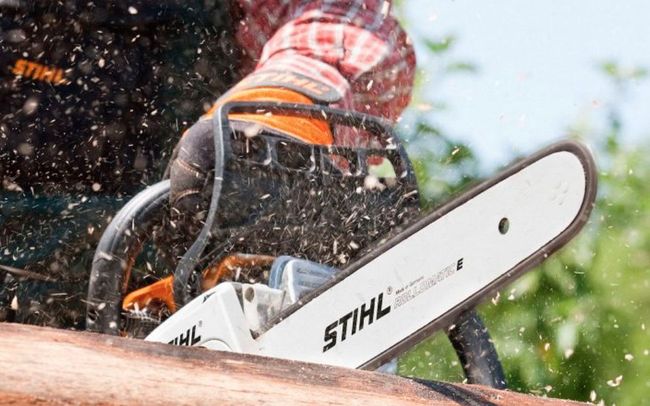 Un ouvrier utilise une tronçonneuse STIHL pour couper du bois, de la sciure vole à l'extérieur.