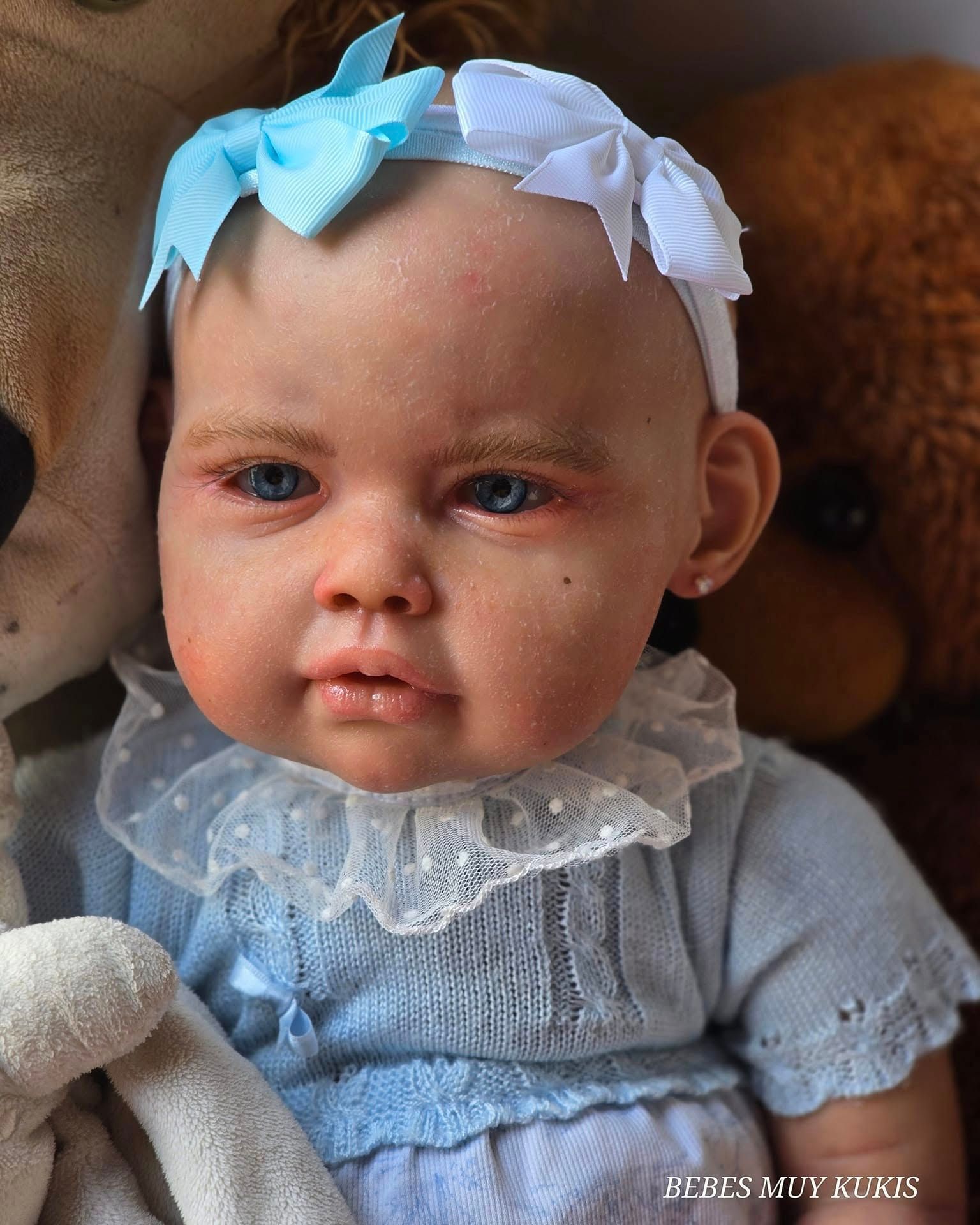 Un muñeco con una diadema azul está sentado junto a un osito de peluche.