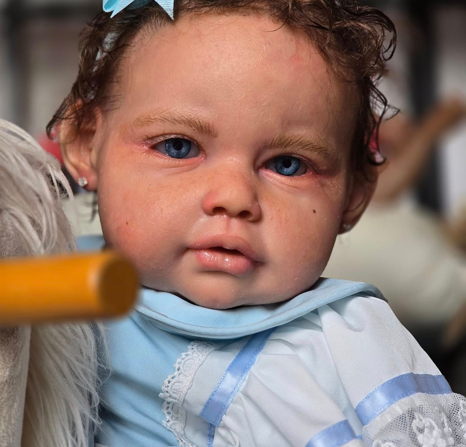 Una muñeca con ojos azules está sentada en un caballo mecedor.