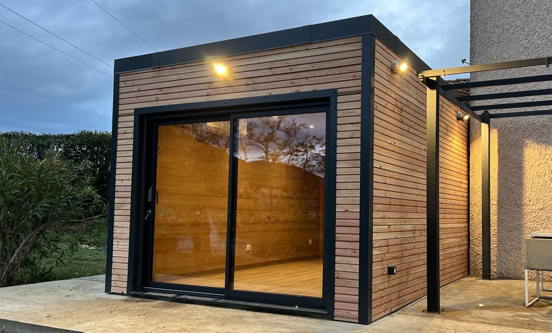 Une cabine en bois moderne avec de grandes portes coulissantes en verre et des garnitures noires, éclairée par des lumières extérieures.