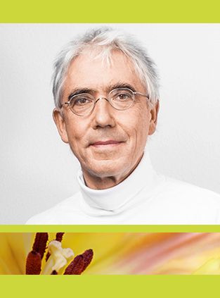 Eine Person mit grauen Haaren und Brille, die einen weißen Rollkragenpullover trägt