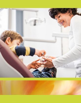 Eine Zahnärztin lächelt, während sie mit einem jungen Patienten interagiert, der auf dem Zahnarztstuhl sitzt.