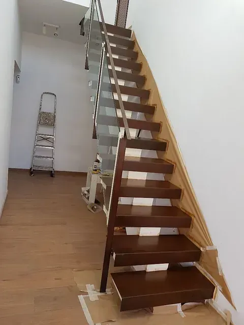 Una escalera de madera con barandilla de metal en un pasillo.