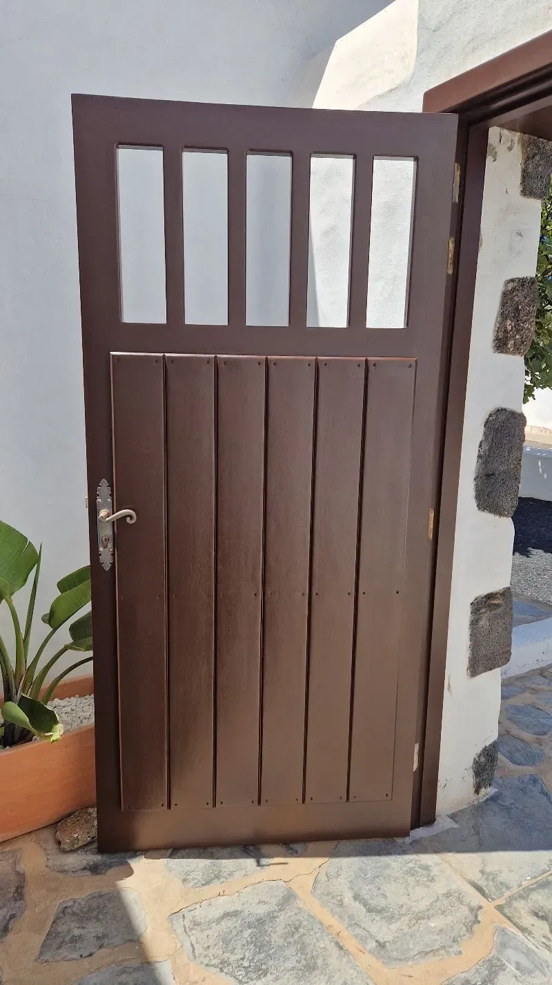 Una puerta de madera marrón con una ventana de vidrio se abre a una pared blanca.