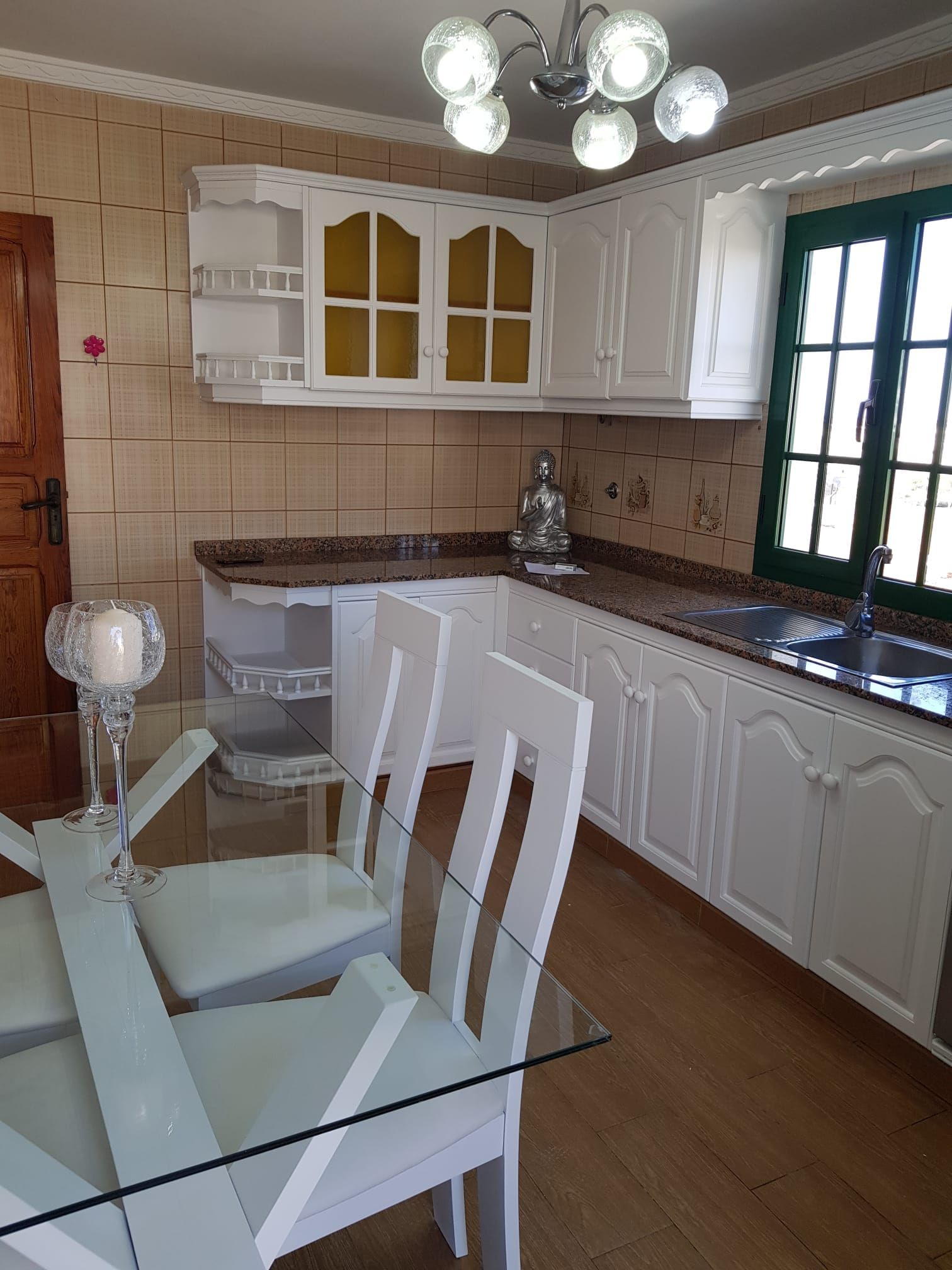 Una cocina con gabinetes blancos y una mesa y sillas de vidrio.