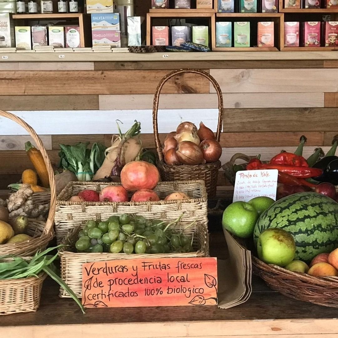 Exhibición de frutas y verduras frescas en cestas en una tienda local con un estante de madera al fondo.