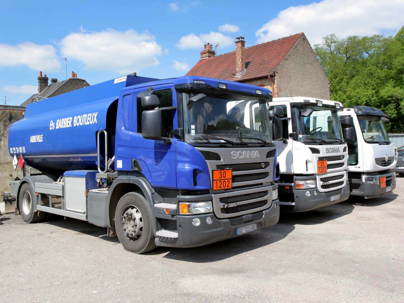 Trois camions-citernes Scania sont stationnés sur un terrain devant un bâtiment en briques.