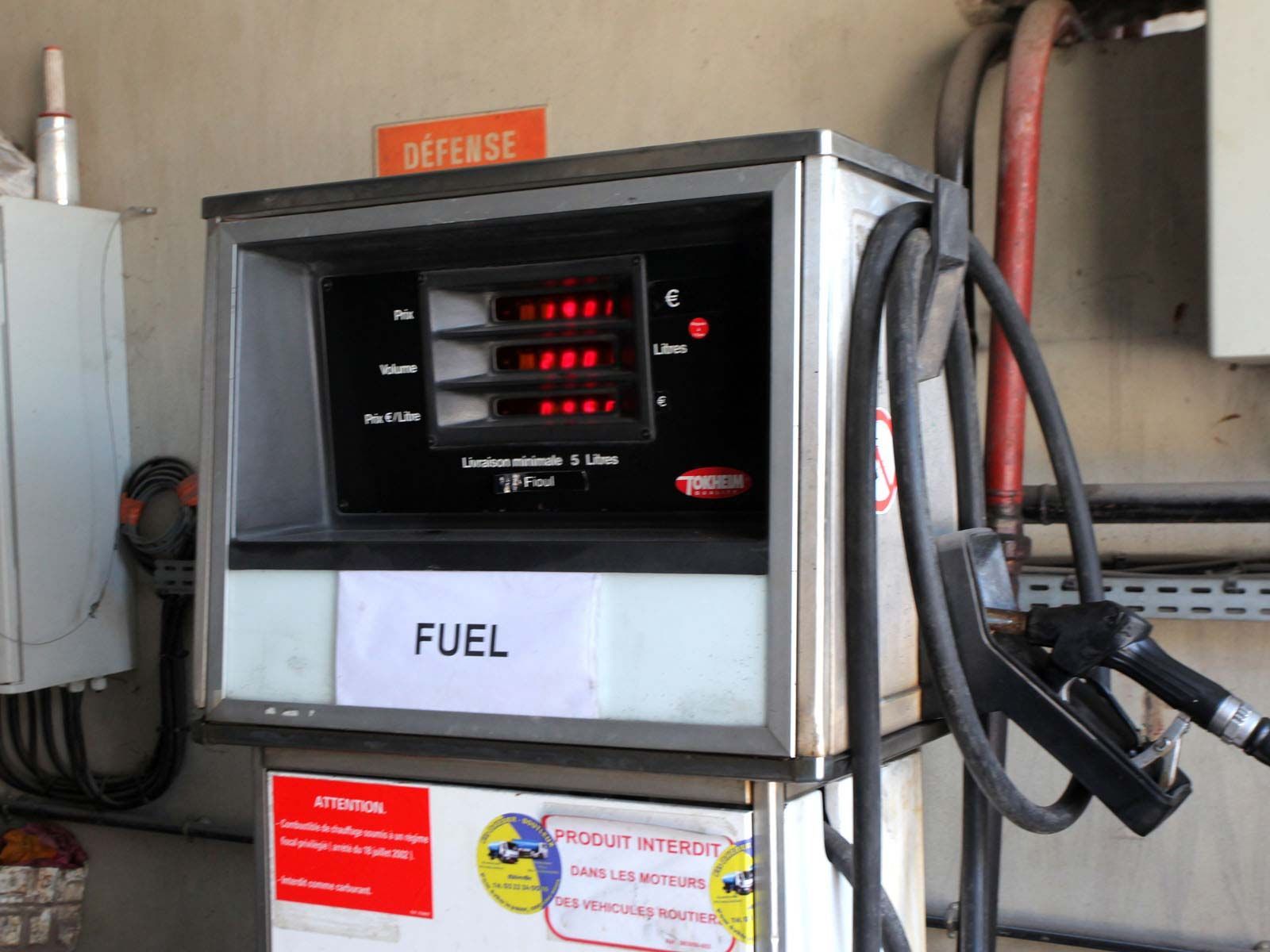 Une pompe à essence argentée dans une station-service, avec un affichage numérique indiquant des zéros et un panneau CARBURANT sur le devant.