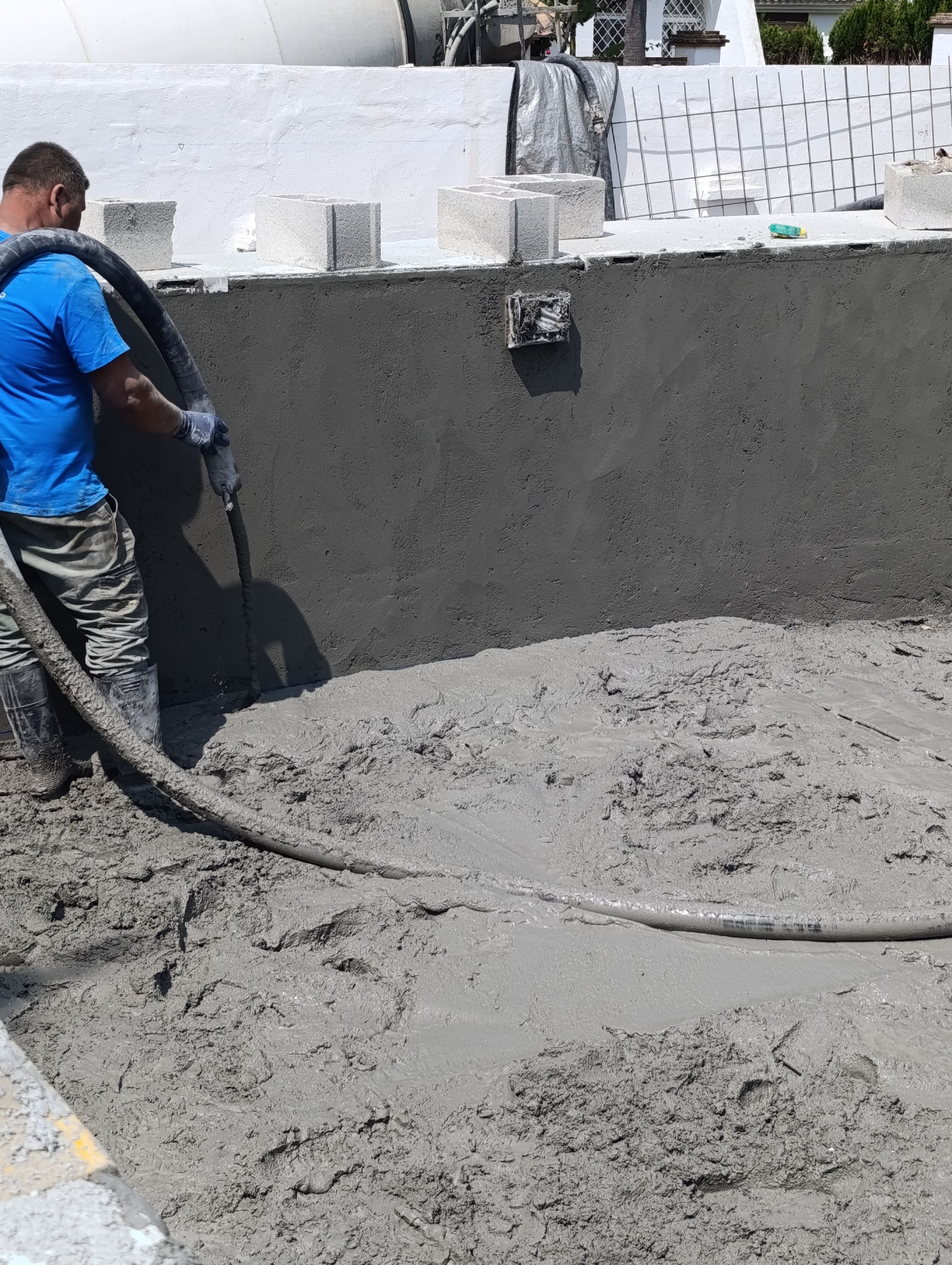 Un hombre está bombeando hormigón a una piscina con una manguera.