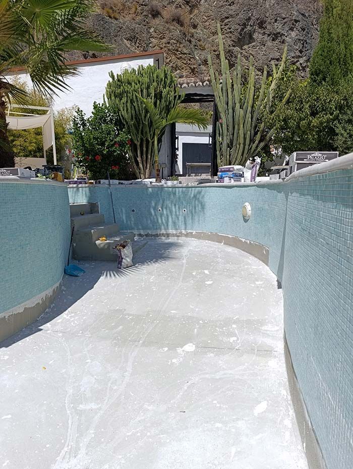 Piscina vacía en proceso de renovación, con azulejos de color azul claro en las paredes y revestimiento blanco en el fondo.