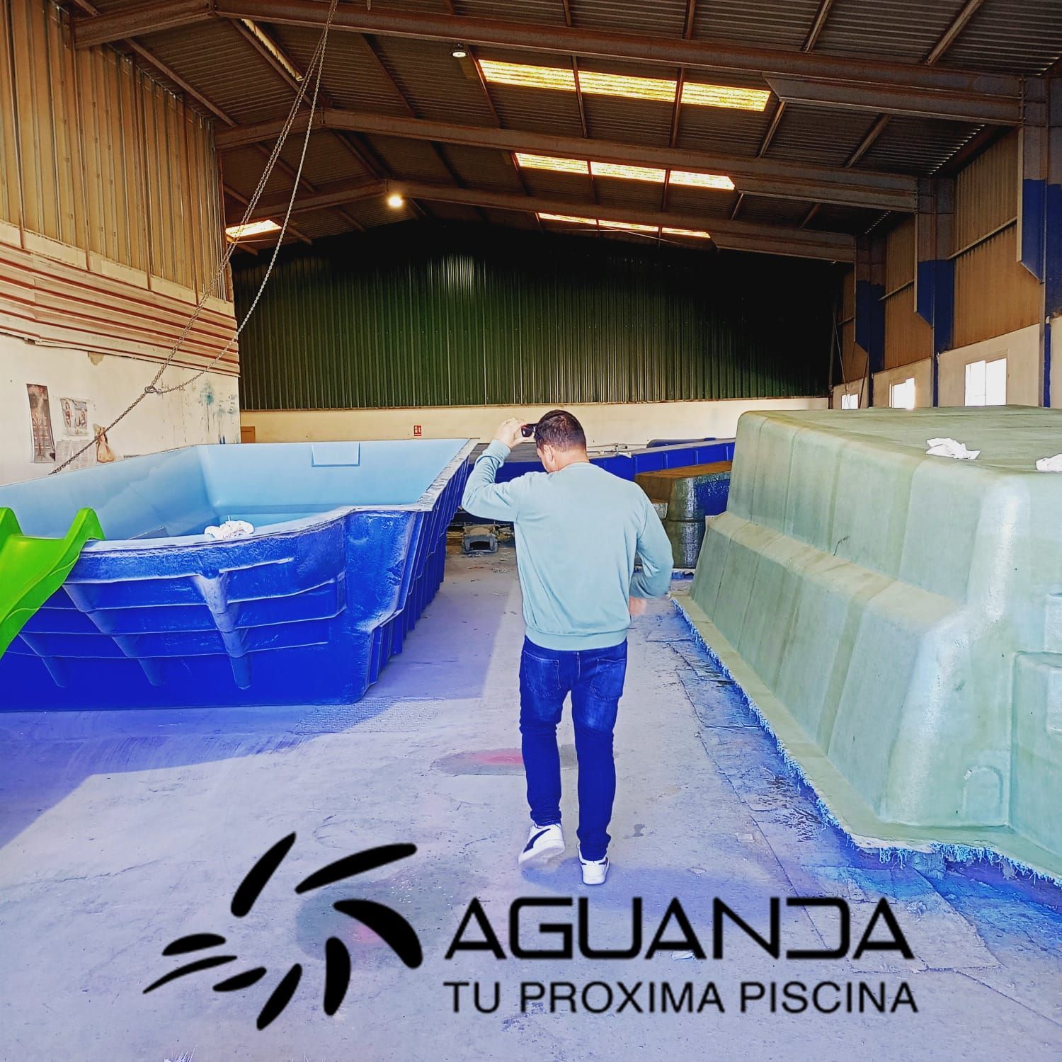 Hombre en almacén con grandes moldes de piscina de fibra de vidrio de color azul y verde, logotipo de Aguanda.