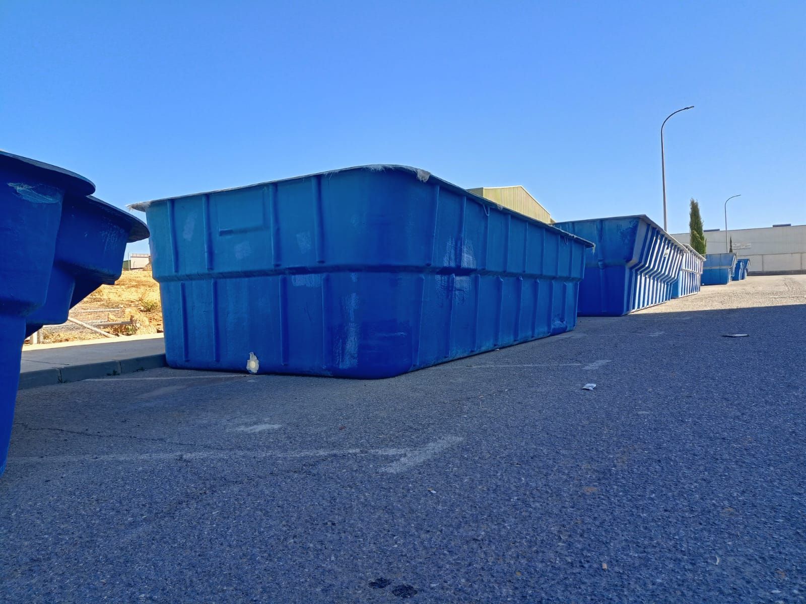 Tanques de plástico rectangulares de color azul sobre asfalto, al aire libre bajo un cielo despejado.