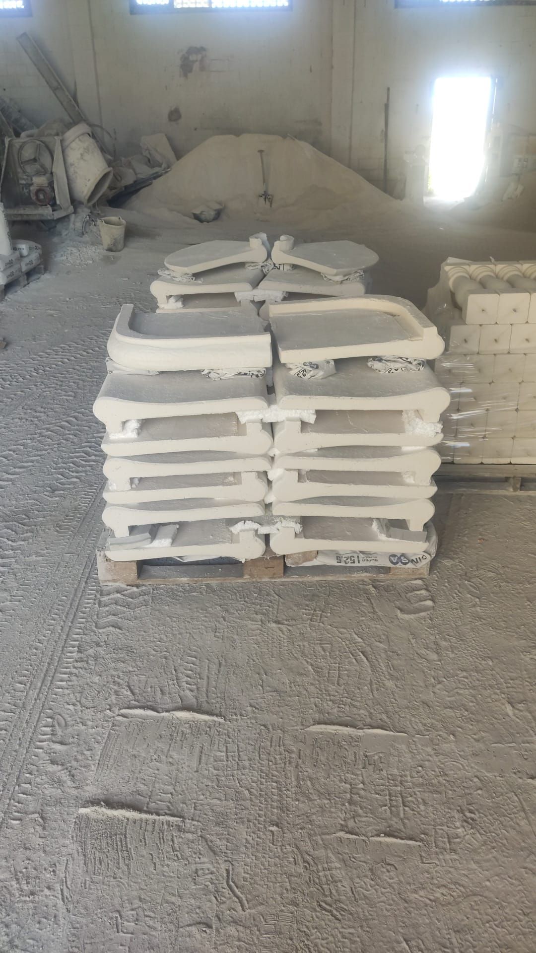 Pila de piezas de piedra blanca moldeada sobre un palé, en una fábrica polvorienta.