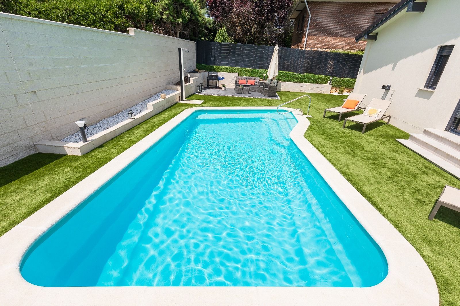 Piscina en patio trasero con tumbonas y zona de patio.