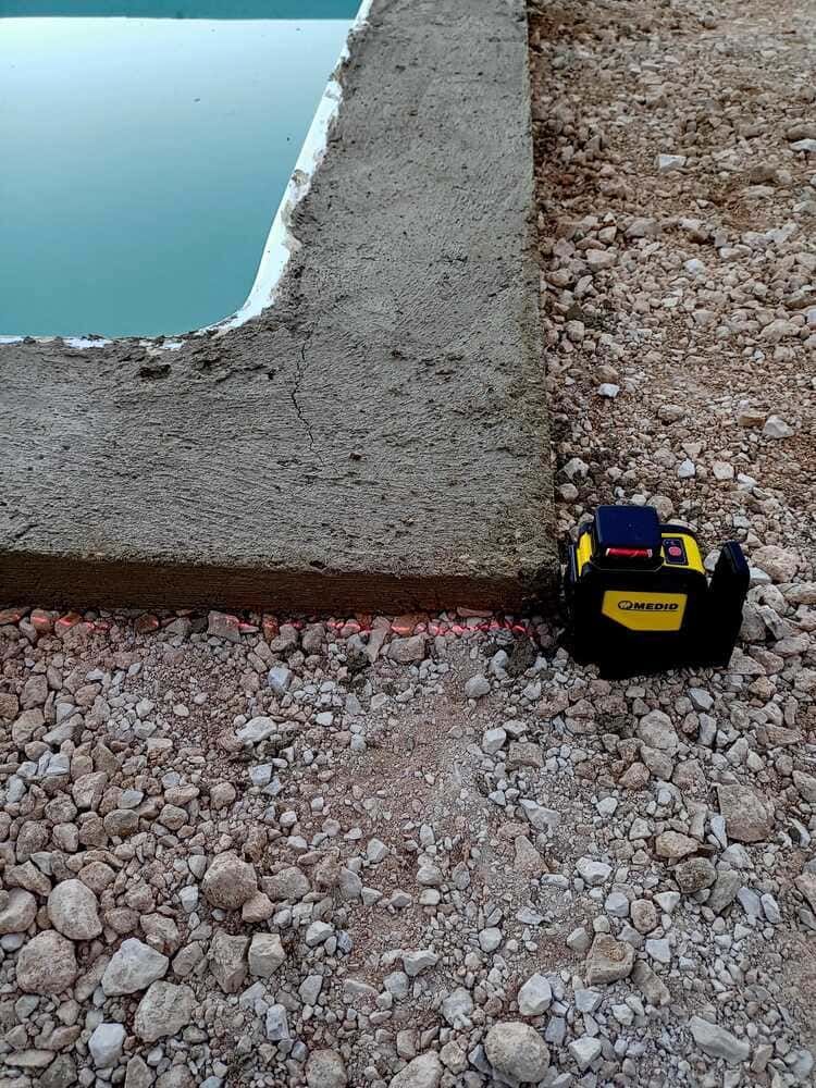 Un nivel láser proyecta una línea roja sobre la grava junto a un borde de hormigón.