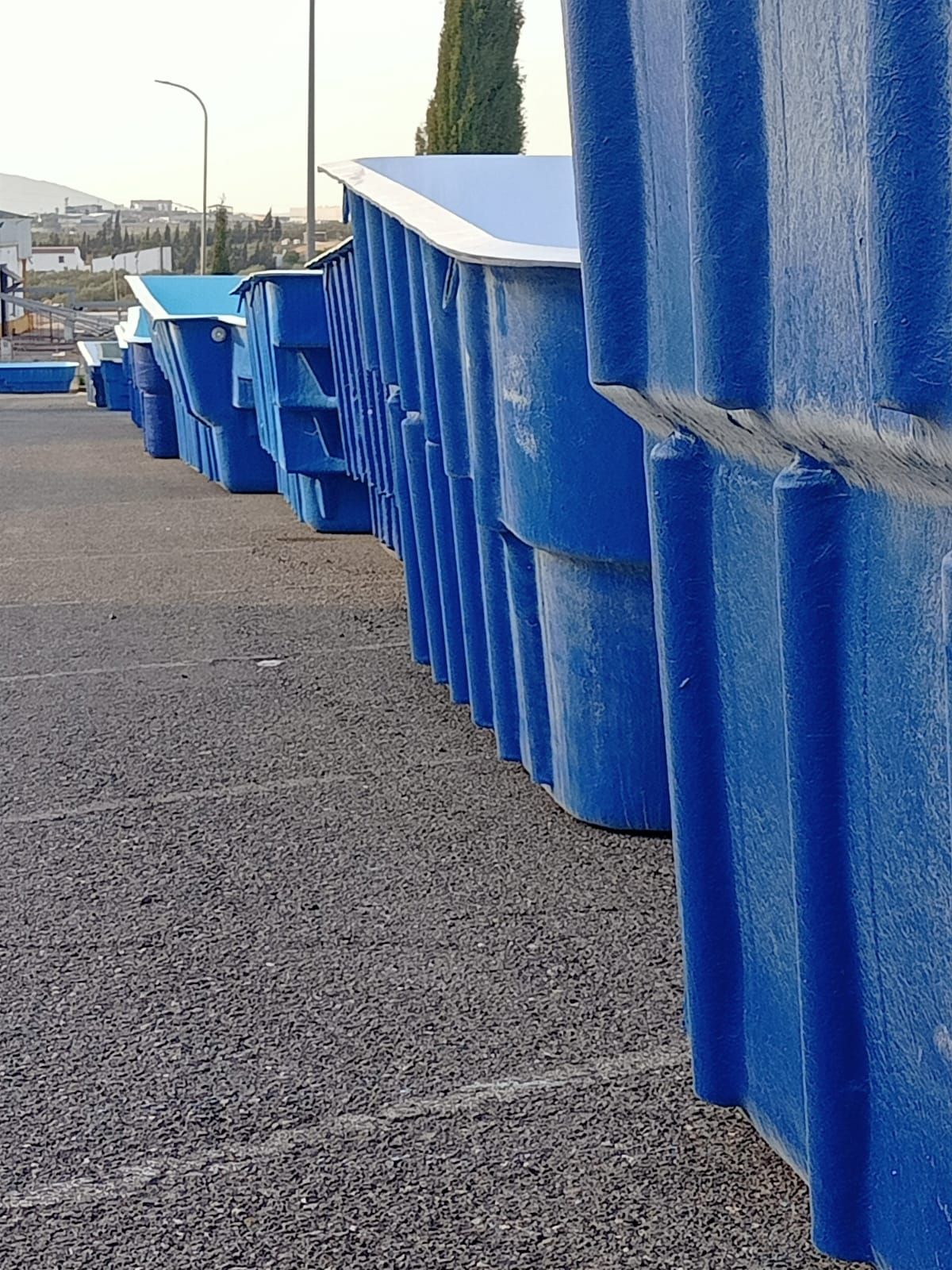 Fila de contenedores de plástico azules apilados sobre el asfalto.