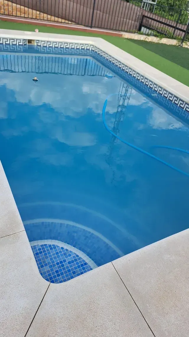 Piscina azul que refleja el cielo, con escalones incorporados y un borde de hormigón de color claro.