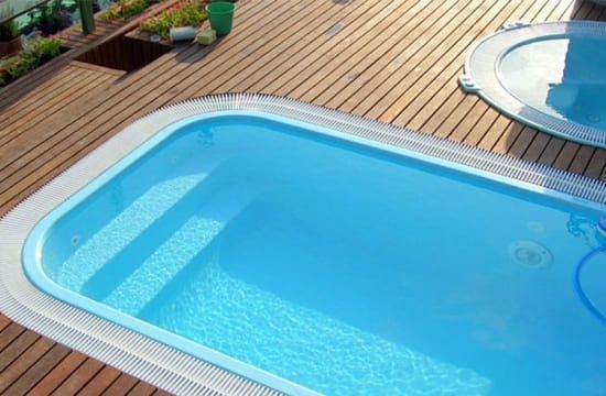 Piscina con agua azul, detalles en blanco y cubierta de madera.