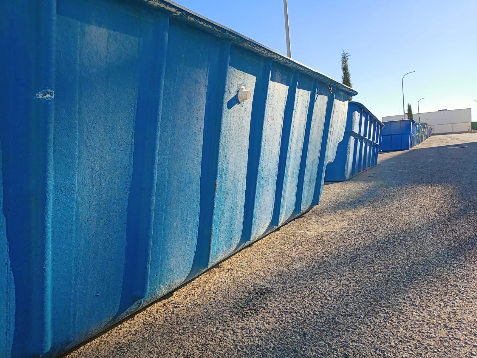 Contenedores industriales azules alineados al aire libre sobre una superficie de grava.