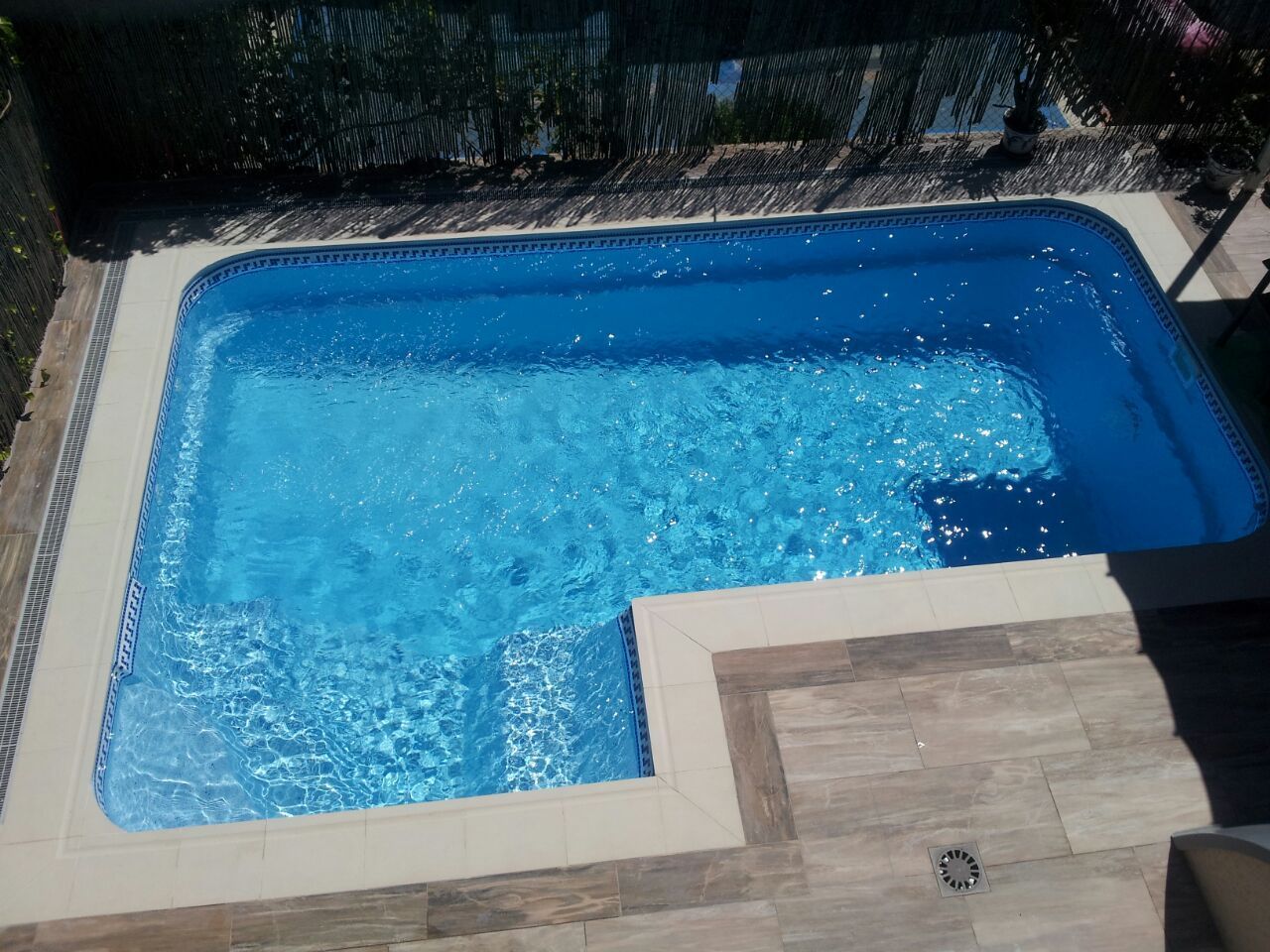 Piscina rectangular azul con escalones. Agua azul claro y cubierta color canela.