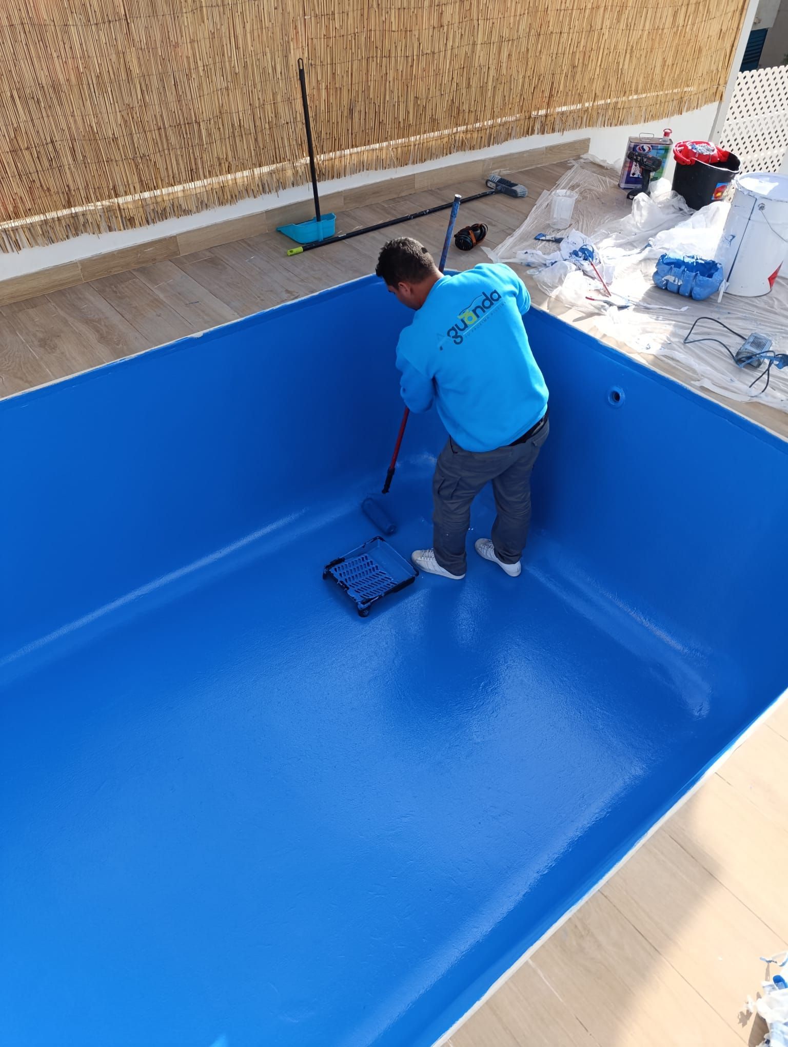 Persona pintando el interior de una piscina azul vacía con un rodillo.