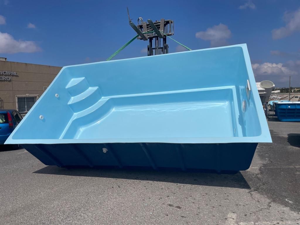 La carcasa rectangular de una piscina de color azul se levanta mediante una carretilla elevadora en un día soleado.
