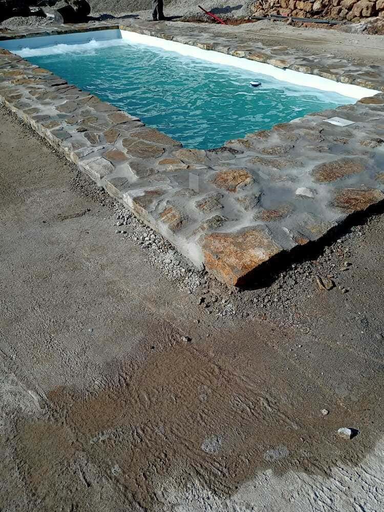 Piscina con borde de piedra, agua turquesa y superficie de hormigón gris.