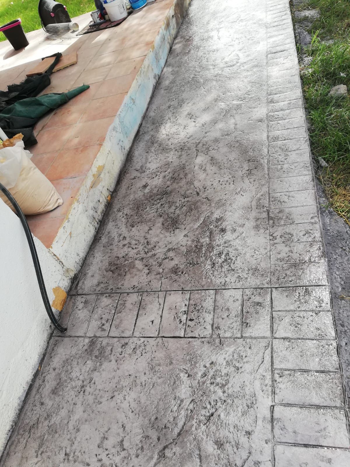 Pasarela de hormigón estampado con acabado texturizado y borde tipo ladrillo junto al césped.