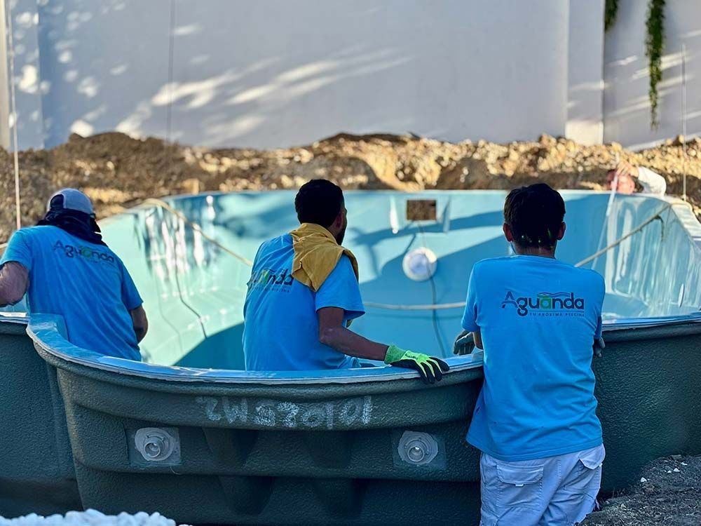 Tres personas con camisas azules instalando una piscina de color azul claro, en el exterior.