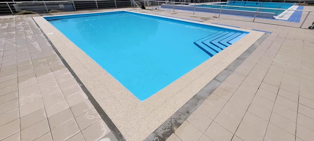 Una piscina al aire libre de agua azul. El área circundante tiene azulejos beige.