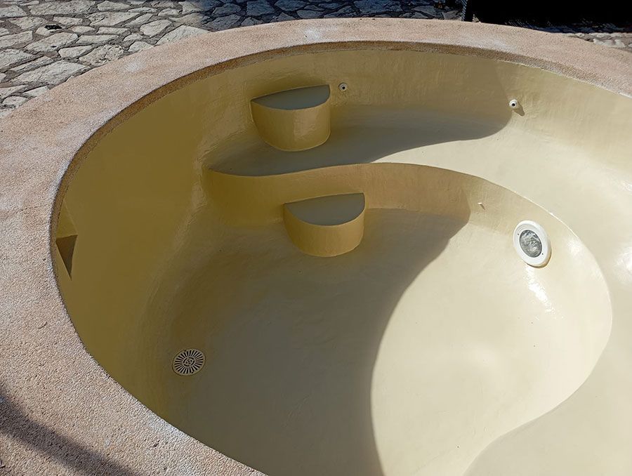 Piscina vacía de color amarillo con escalones y chorros incorporados, rodeada por un borde de piedra.